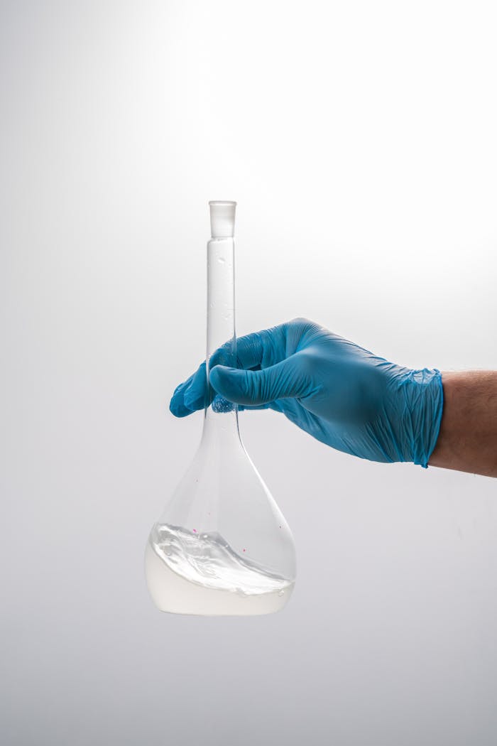 Close-up of a gloved hand holding a volumetric flask in a scientific laboratory setting.